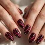 Polka dot cat eye nails in deep burgundy with a velvet magnetic shine and neat white dots